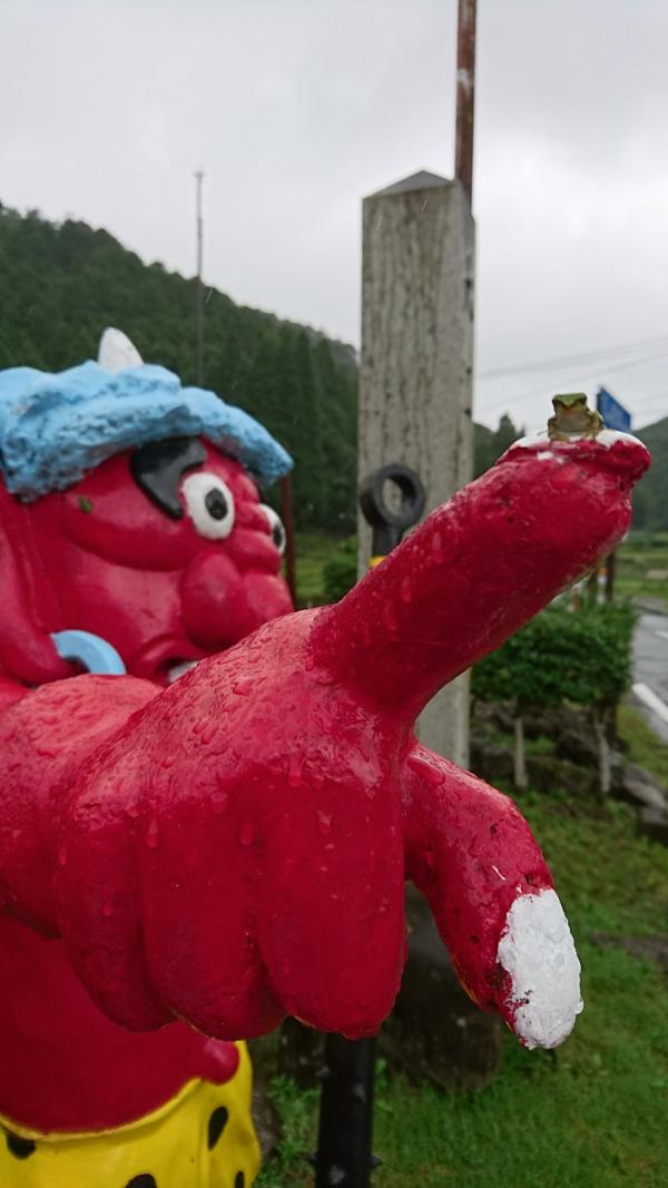 赤鬼の像の指先に座るカエルの画像