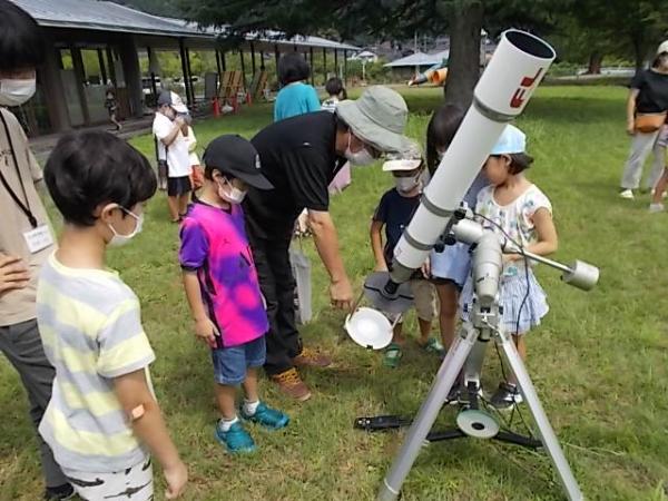 望遠鏡が太陽を写したものを子どもたちが見ている様子です