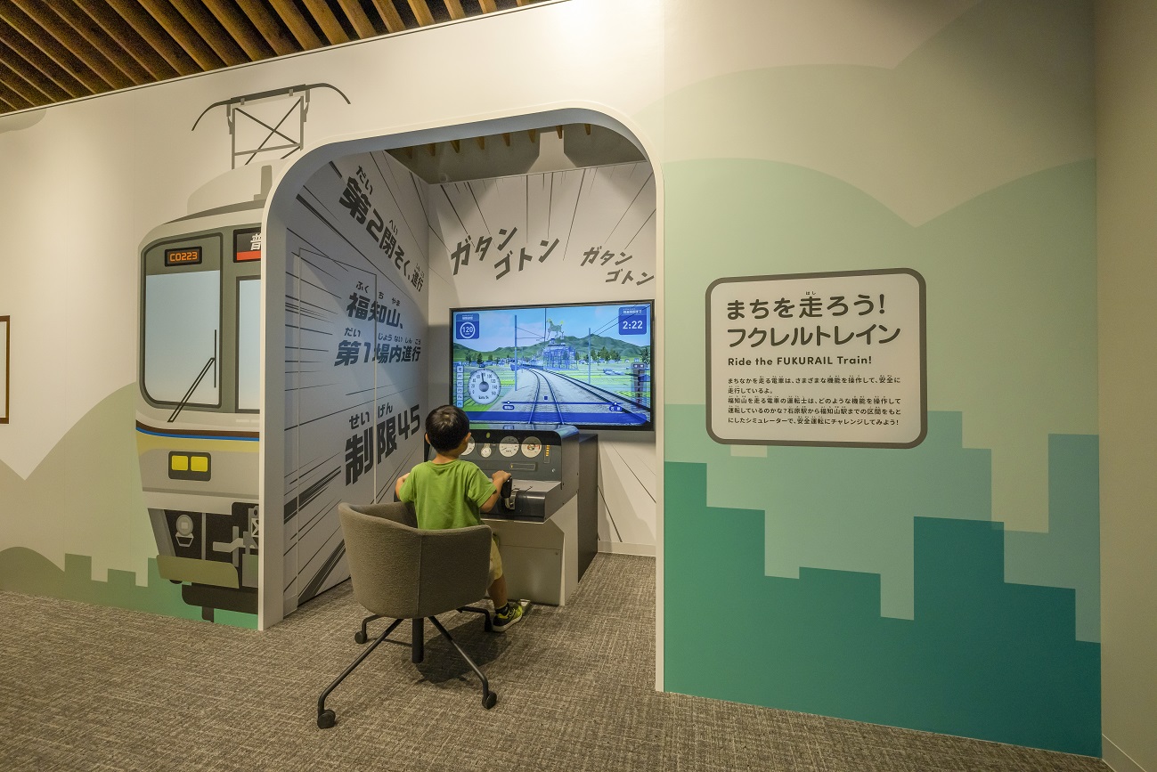 施設の内部、こどもが運転シミュレーターで遊んでいる後ろ姿。