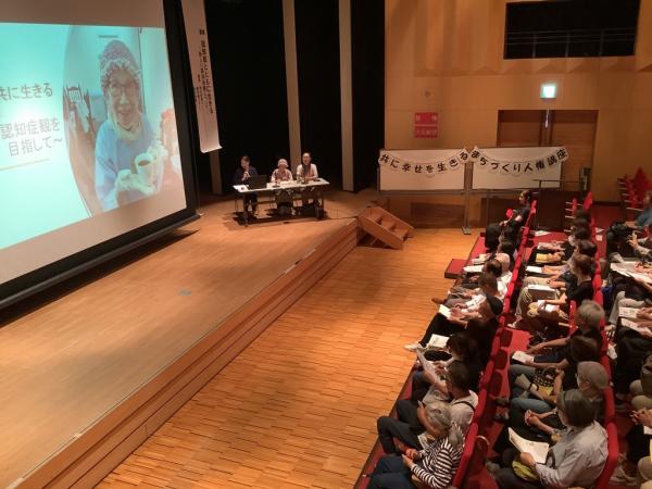 舞台の上で鈴木さんとご家族の方と包括支援センターの方が講演をしている様子です