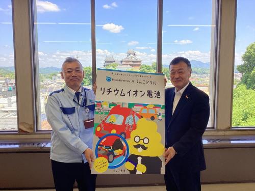 うんこドリルのパネルを手に並ぶ中村社長と廣田教育長の写真